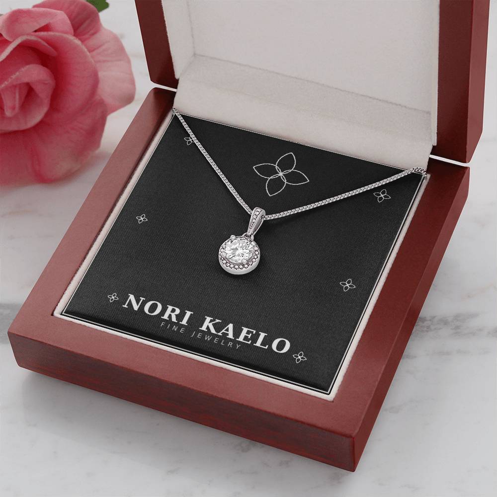 Halo pendant necklace displayed in an open mahogany gift box, styled with a pink rose in the background.