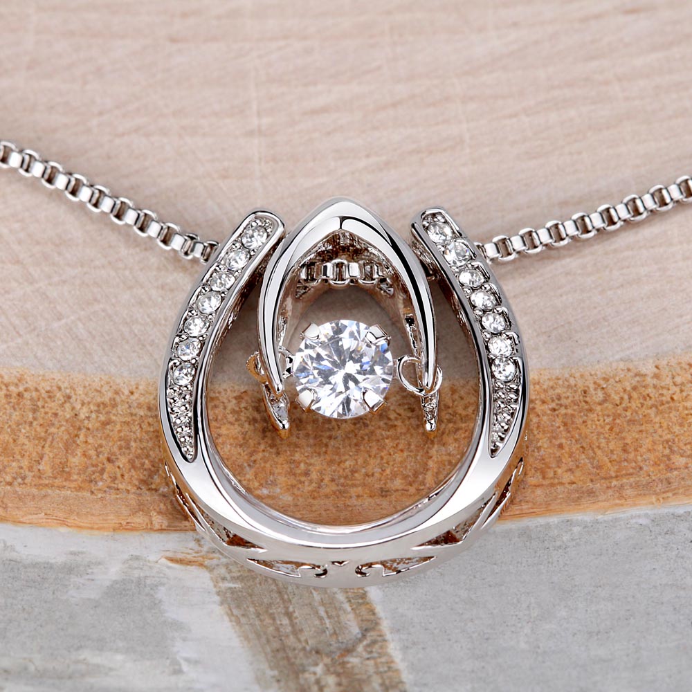 Close-up of a dancing stone pendant in white gold, set against a sandy beige background.