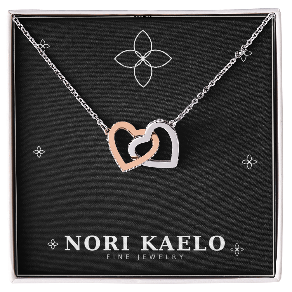 Interlocking hearts pendant necklace in rose gold and white gold, displayed on a black Nori Kaelo Fine Jewelry gift box.